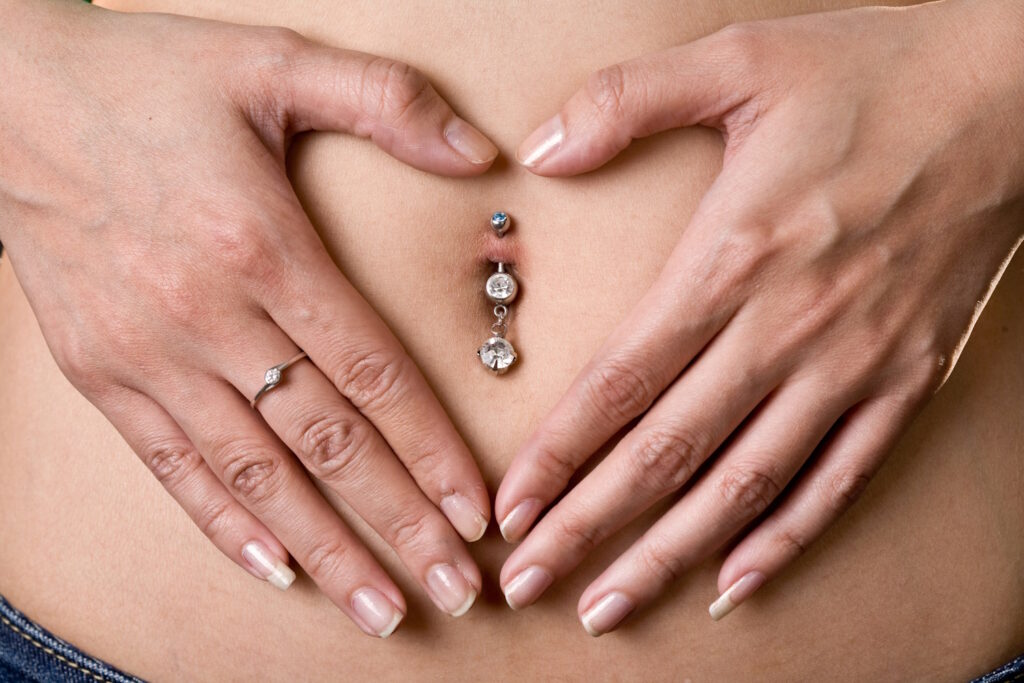 A woman with her hands in a heart shape around her belly button piercing.
