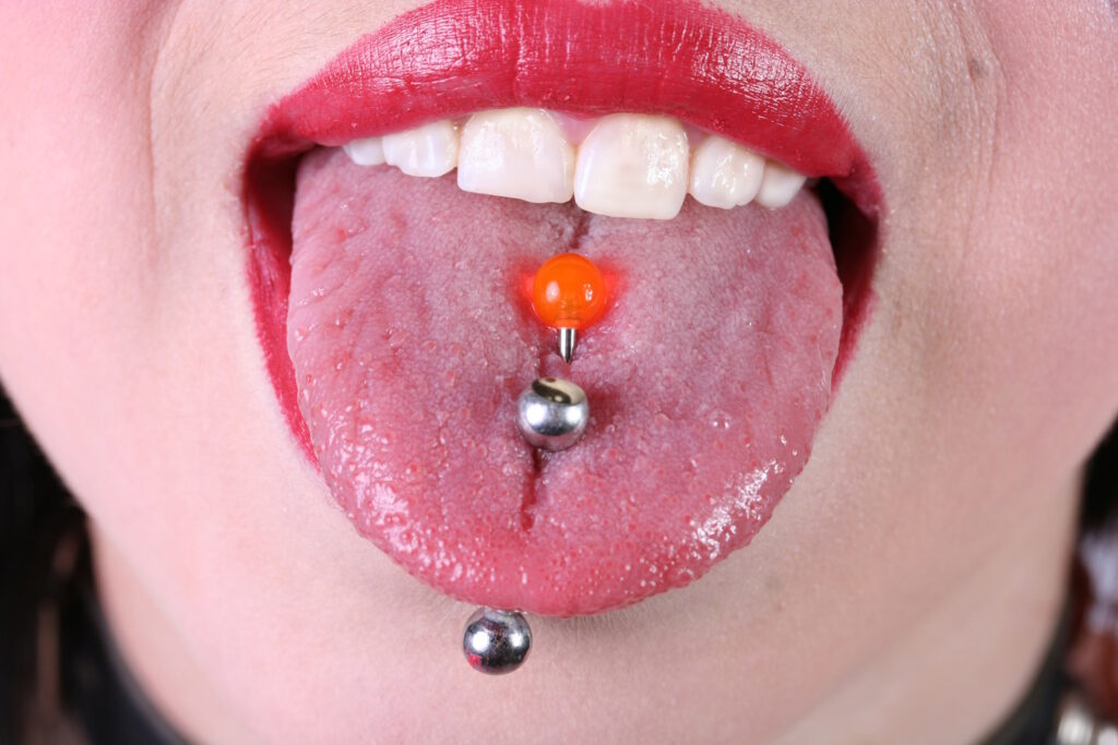 A woman with bright red lipstick sticking out her tongue with a double tongue piercing.