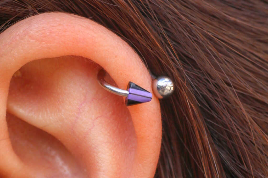 A healed helix piercing with a circular barbell that has purple spikes.