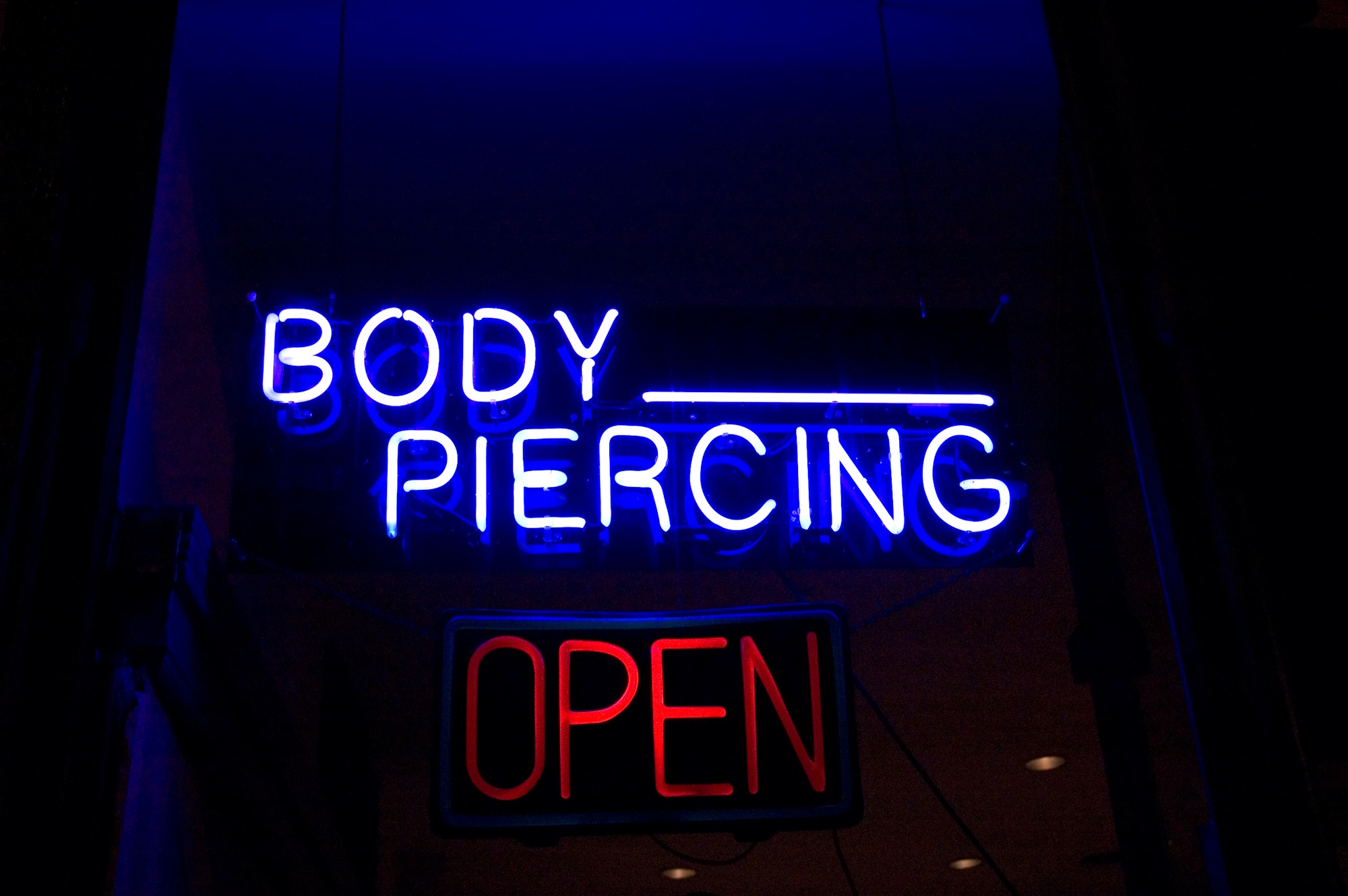 A body piercing studio neon sign that has BODY PIERCING in blue neon and OPEN in red neon.