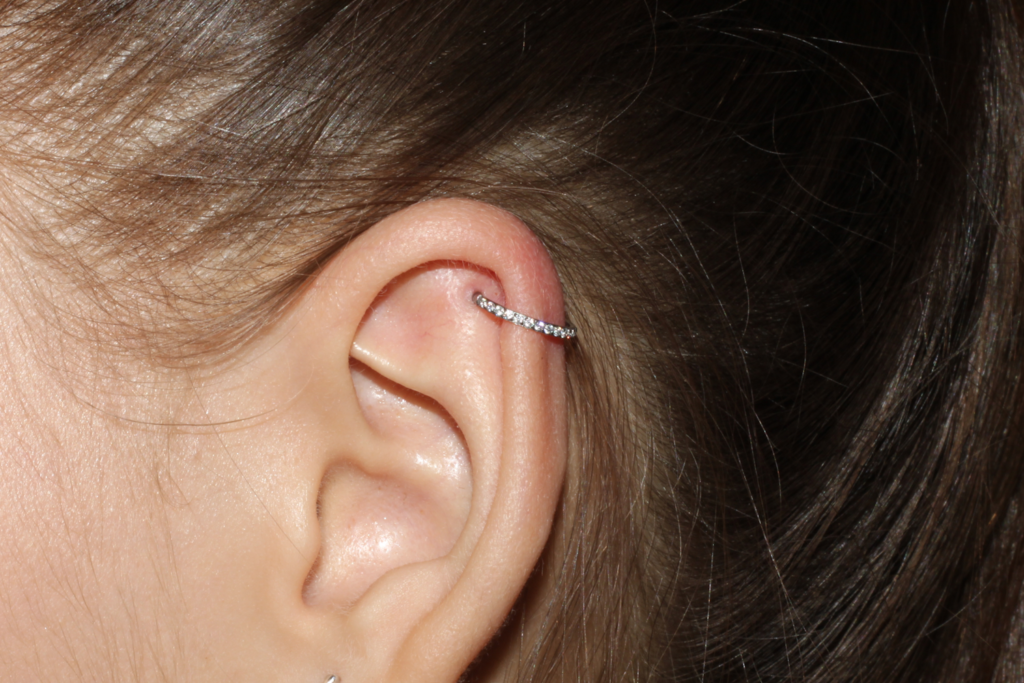 A woman with long hair that has a cubic zirconia cartilage hoop in her ear.