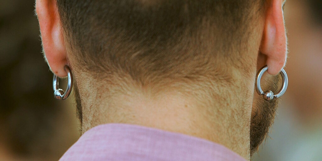 A man viewed from the back with earlobe piercings in his ear.