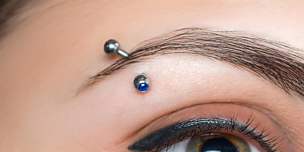 Woman with eyeshadow and an eyebrow piercing that has a curved barbell in it.