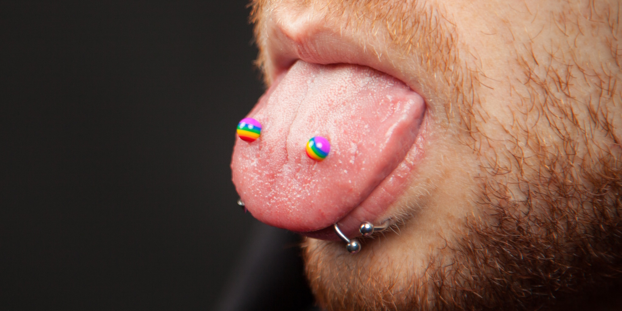 A man displaying a frog eyes piercing that has rainbow color balls on the ends of his tongue bars.