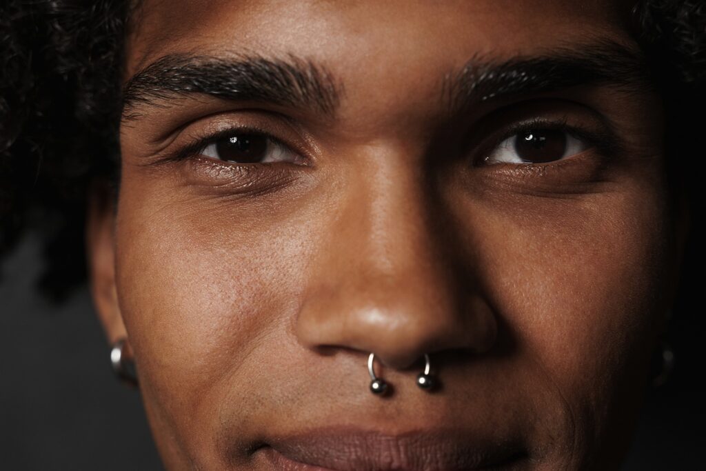 A close up of a man's face with a large septum ring in his septum piercing. 