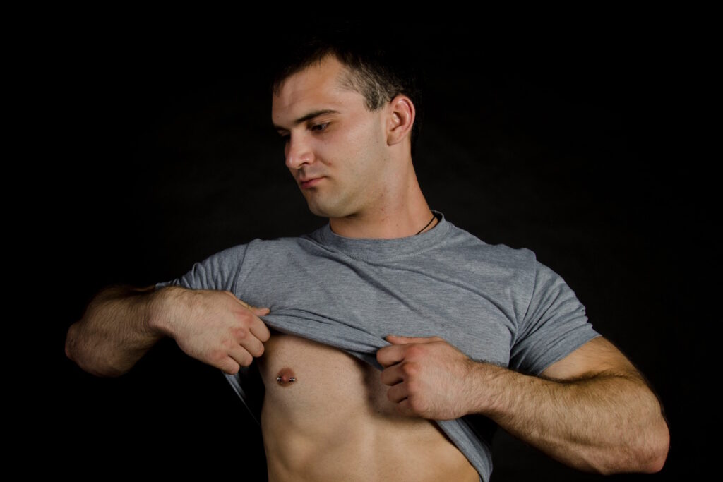 A man with his shirt lifted showing off this nipple piercing.
