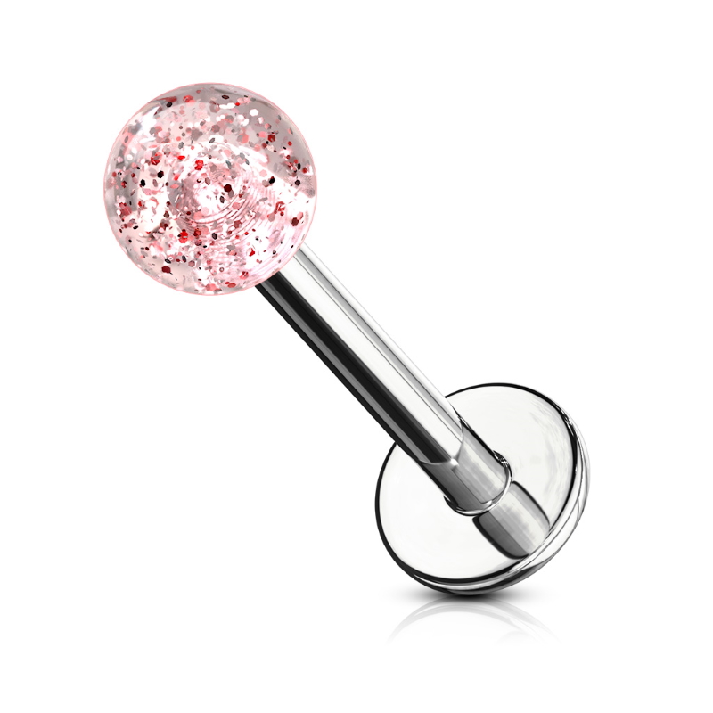 A type of body jewelry known as a labret with a red sparkle glitter ball pictured against a white background.