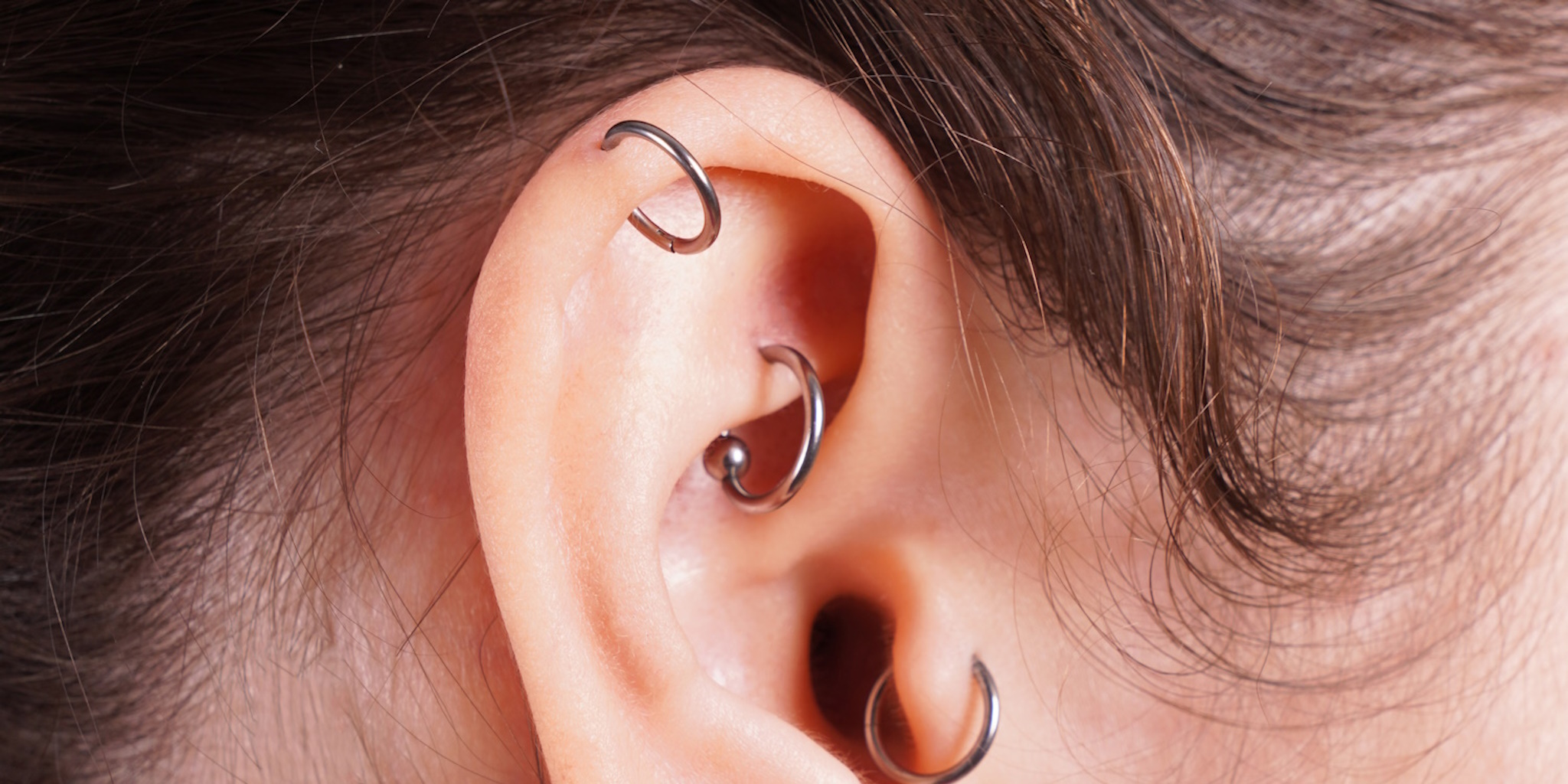 A female with a rook piercing, cartilage piercing, and tragus piercing.