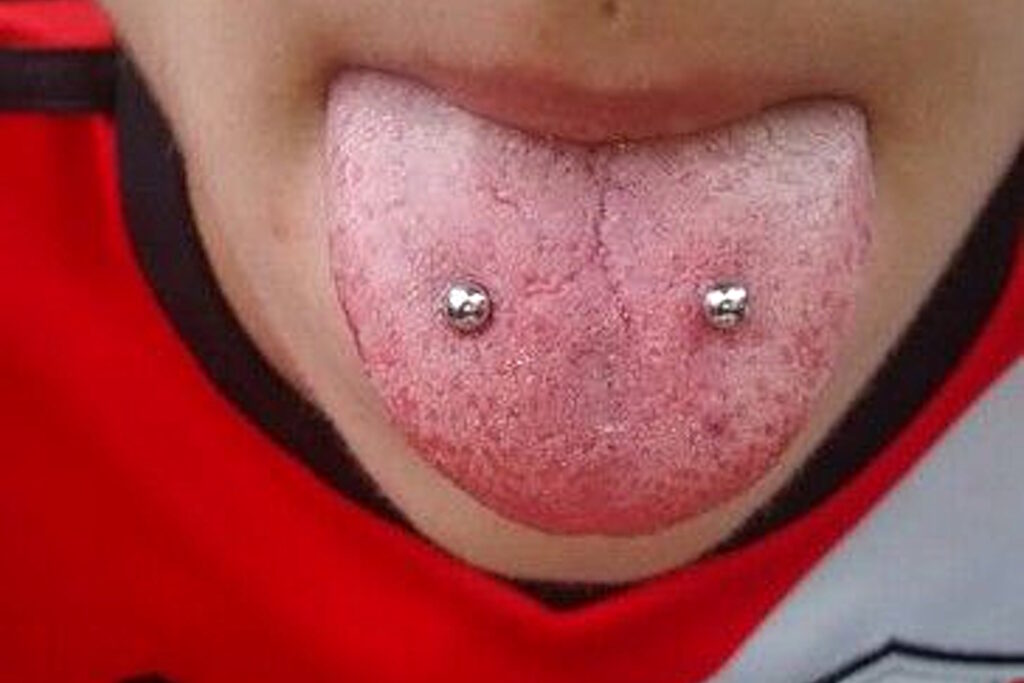 Woman in a red shirt sticking out her pierced tongue.
