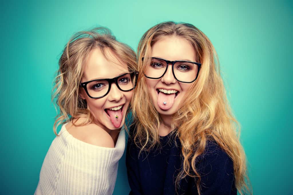 Two women that both are sticking out their tongues and showing off their tongue piercings.